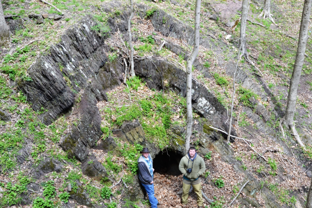 two students stand next to a cave and geological formation